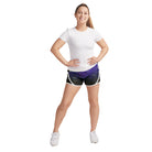 Model wearing S‑Line paneled performance shorts in black with white piping trim and purple geometric panel, mid-rise fit with elastic waistband—styled for dance, drill, or color guard